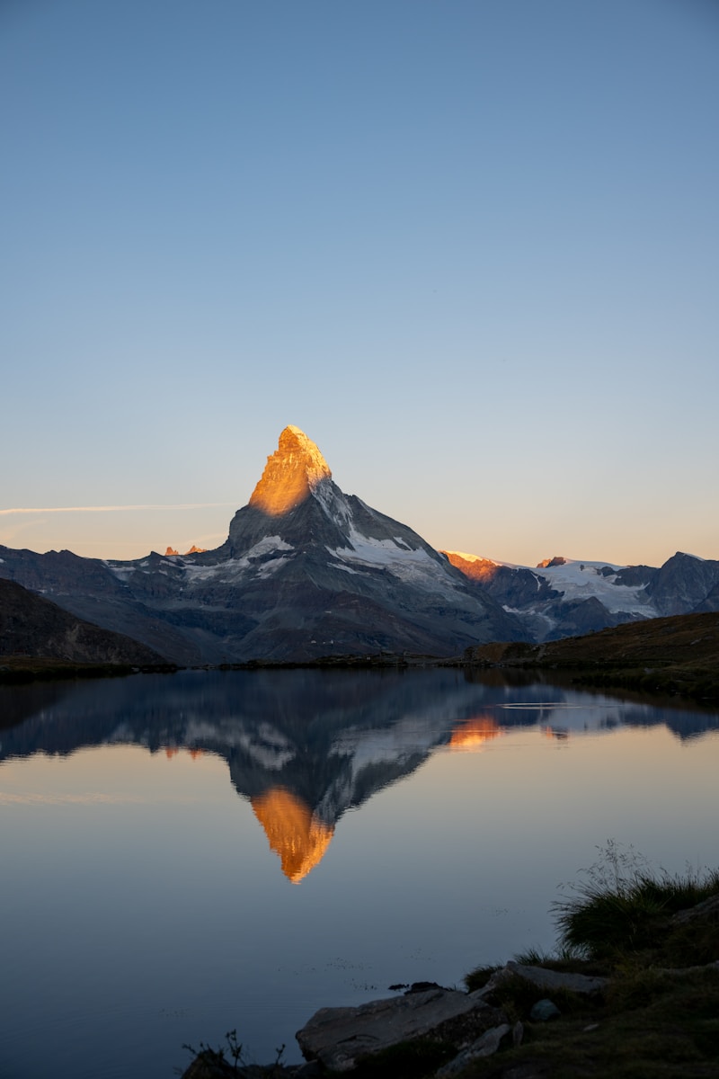 Mountain peak reflecting in calm lake at sunrise.
