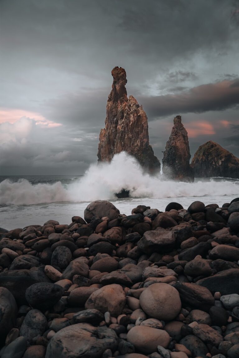 Waves crash against rocky sea stacks under cloudy sky.