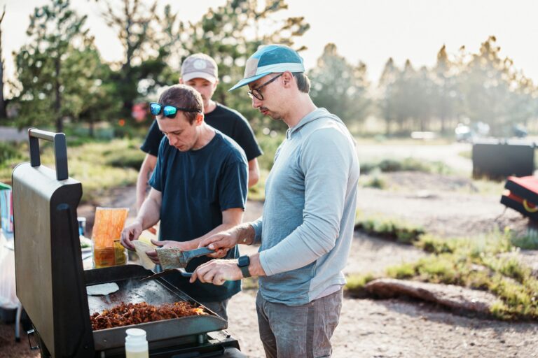 Three men cooking food on an outdoor grill.