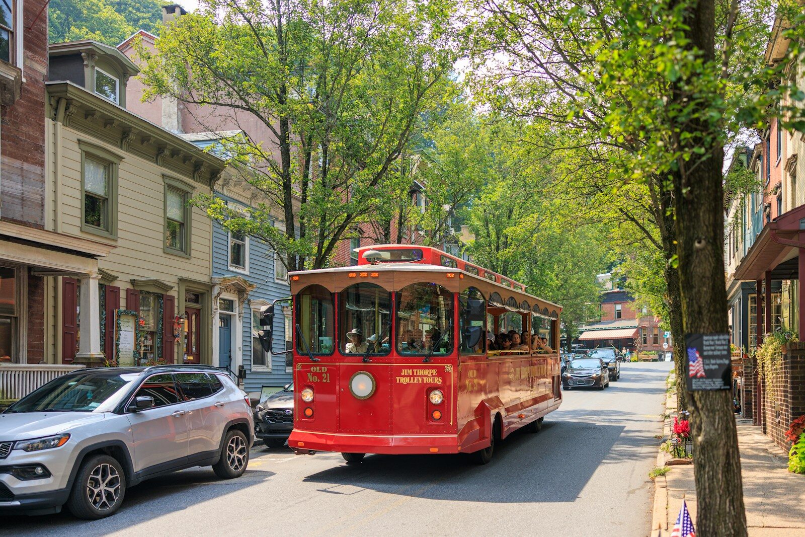 Red trolley car driving down a tree-lined street.